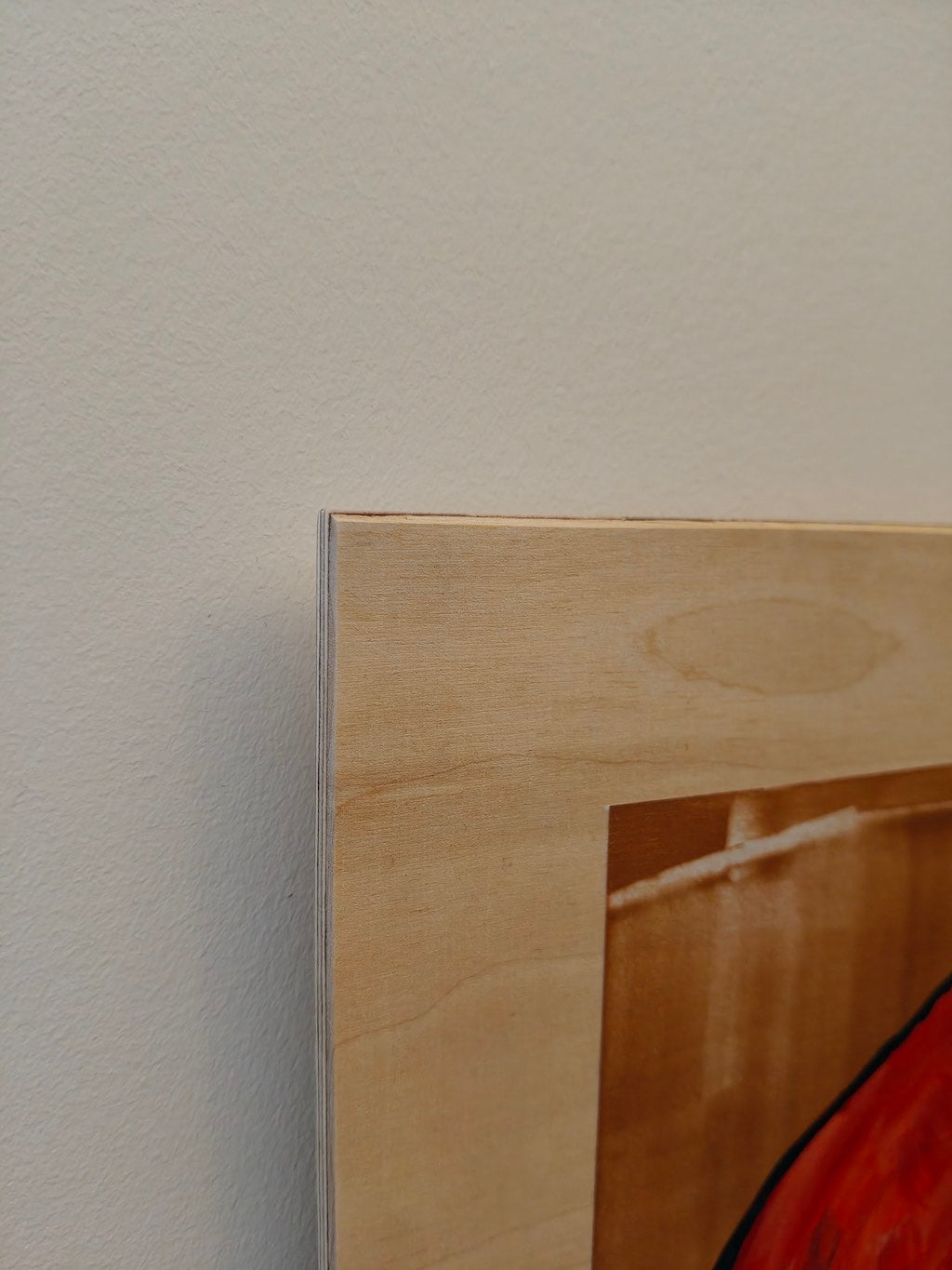 Close up of acrylic paint on birch plywood showing the wood material, and a small section of the painting itself with orange and gold.