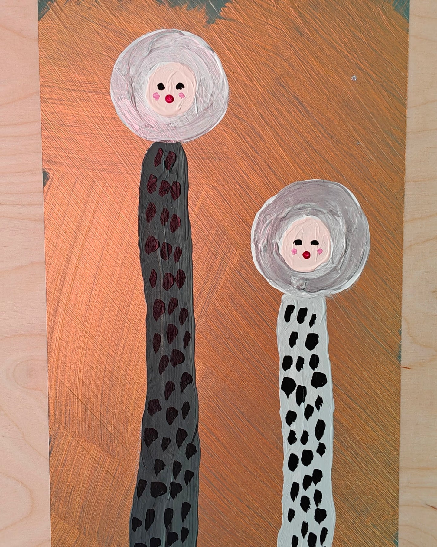 A playful painting featuring two tall, abstract figures with dotted bodies and round, expressive faces. The background has a metallic copper tone, contrasting with the natural plywood that the image has been painted on. Part of the Life in Colour collection.