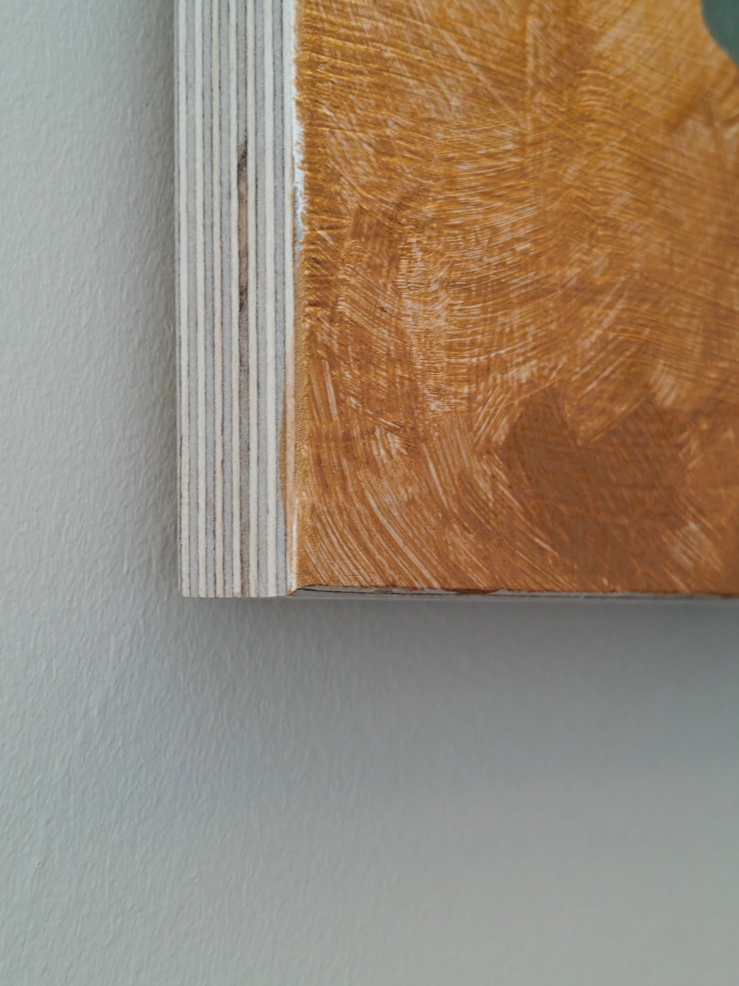 Close up of a painting on plywood, against a white wall. The image shows the corner of the painting, which has a gold background.