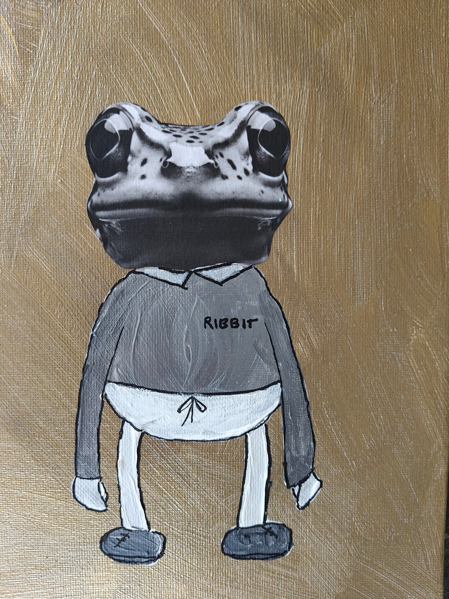 Close up of a Playful mixed media painting of a frog dressed in a sweater, trousers and trainers, set against a background of gold. His sweater has the word ribbit written on the chest.