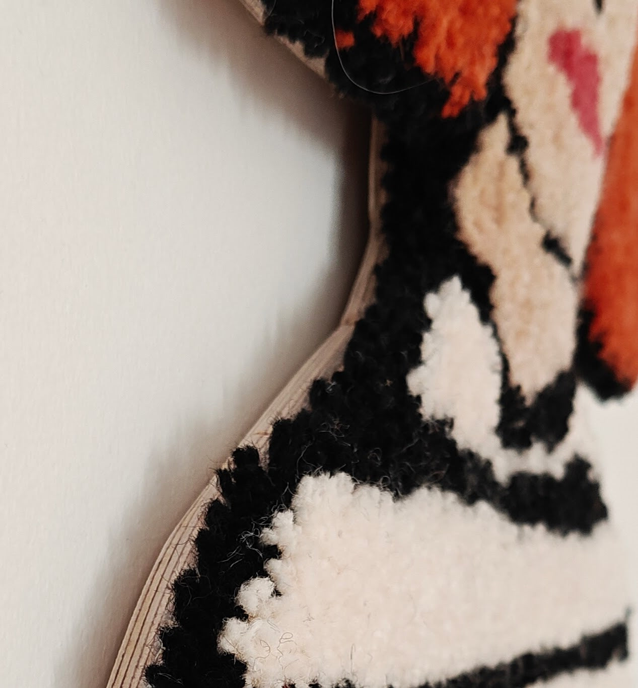 Tufted textile artwork depicting a red-haired woman with a bob haircut, bold black eyebrows, red lips, and a striped shirt, designed in a modern, textured style. Close up showing the plywood that the tufted work has been mounted on.