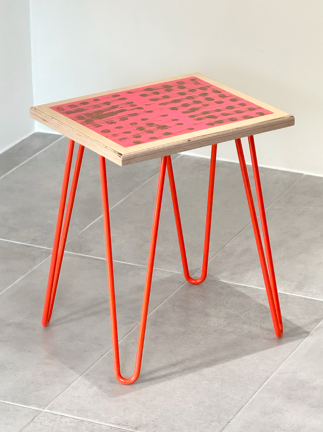 Plywood side table with hand-painted unique design in pink and gold. Orange metal hairpin legs. Side view