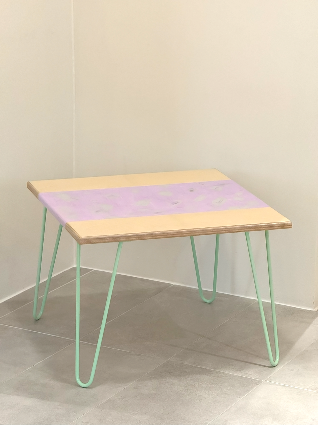 Plywood coffee table with handpainted unique design in purple and grey. Light green metal hairpin legs. Side view