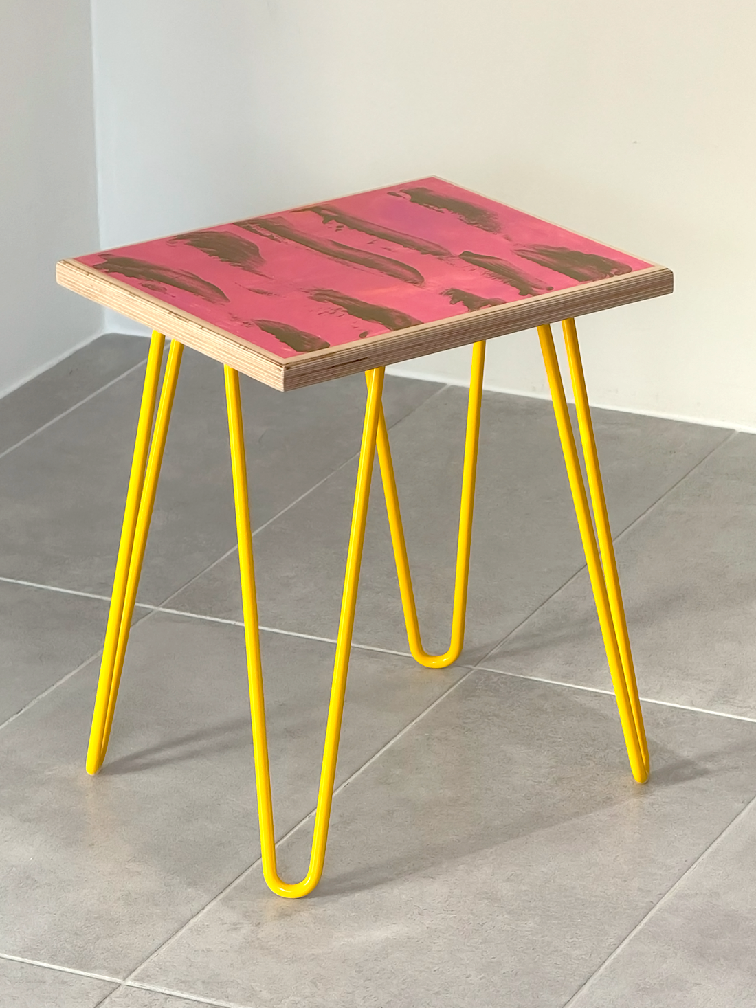 Plywood side table with hand-painted unique design in pink and gold. Yellow metal hairpin legs. Side view