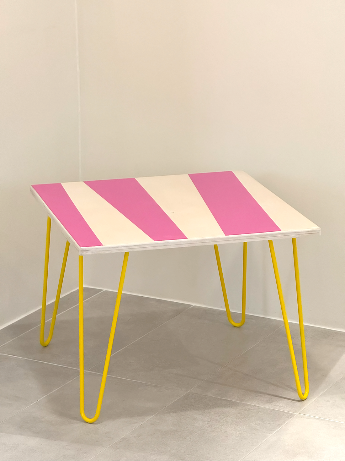Plywood coffee table with handpainted unique design in pink and white. Bright yellow metal hairpin legs. Side view
