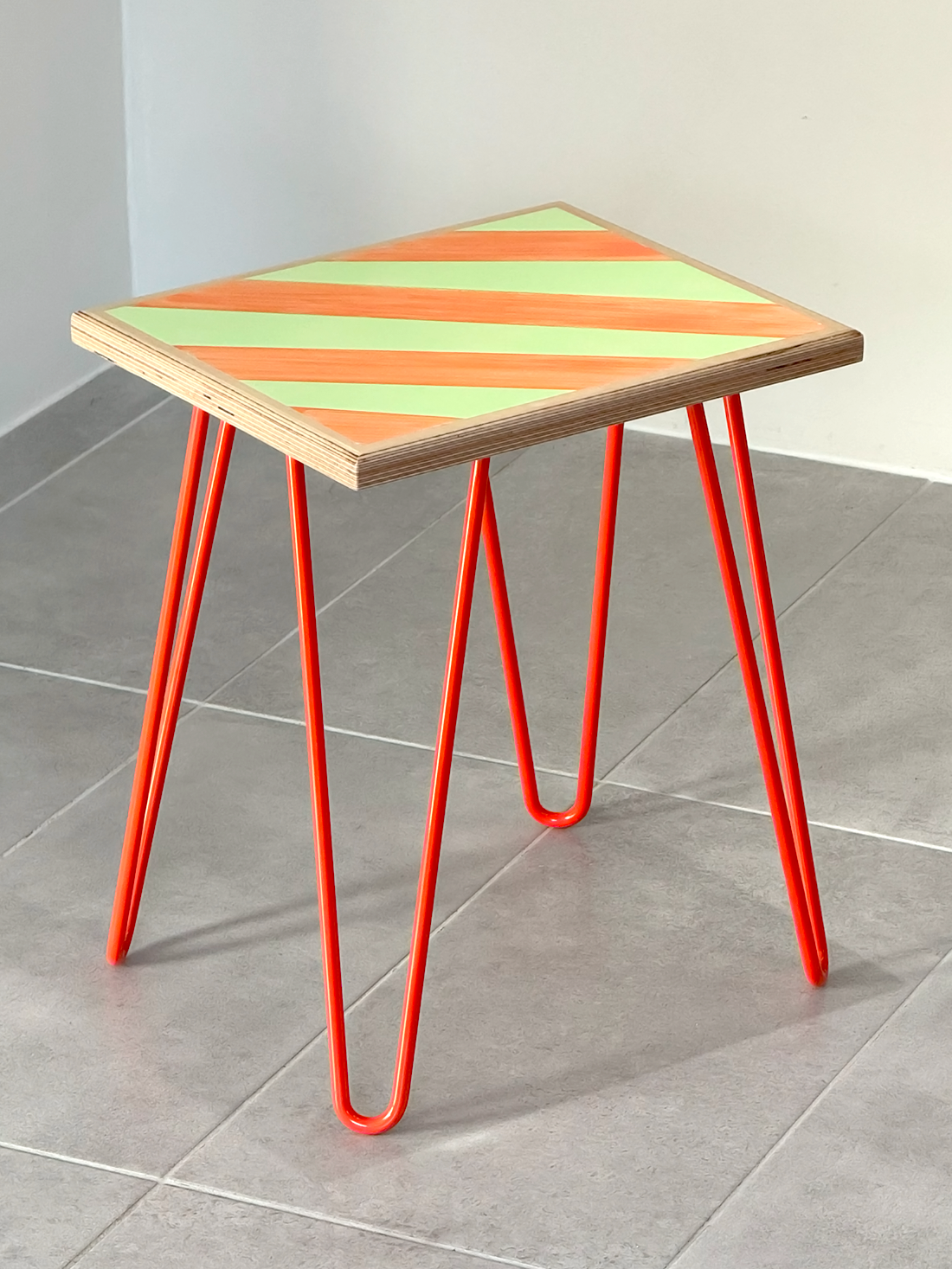 Plywood side table with hand-painted unique design in orange and green. Orange metal hairpin legs. Side view