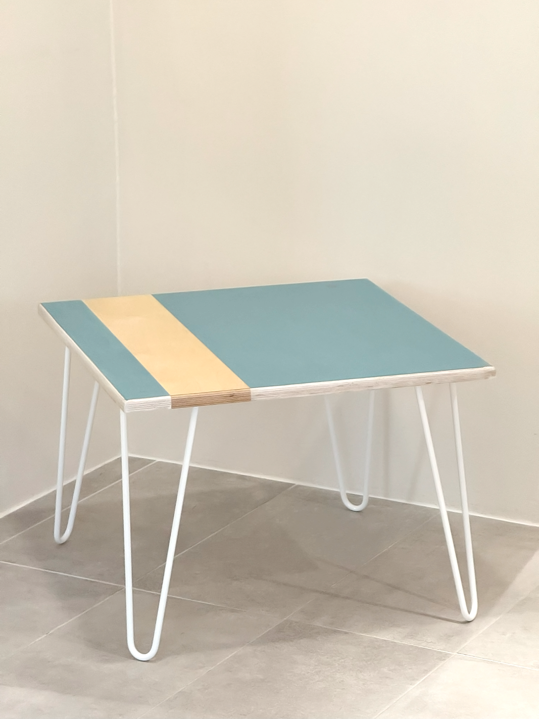 Plywood coffee table with handpainted unique design in blue and white. White metal hairpin legs. Side view