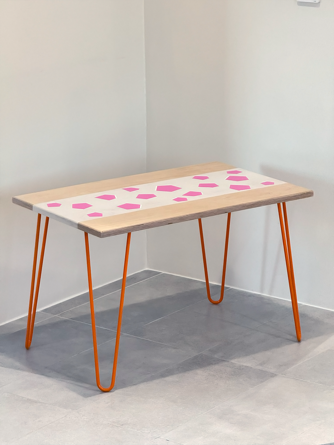 Plywood coffee table with hand-painted unique design in white and pink. Orange metal hairpin legs. Side view. 